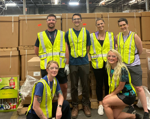 Five people with safety vests on in front of boxes at a community service event.